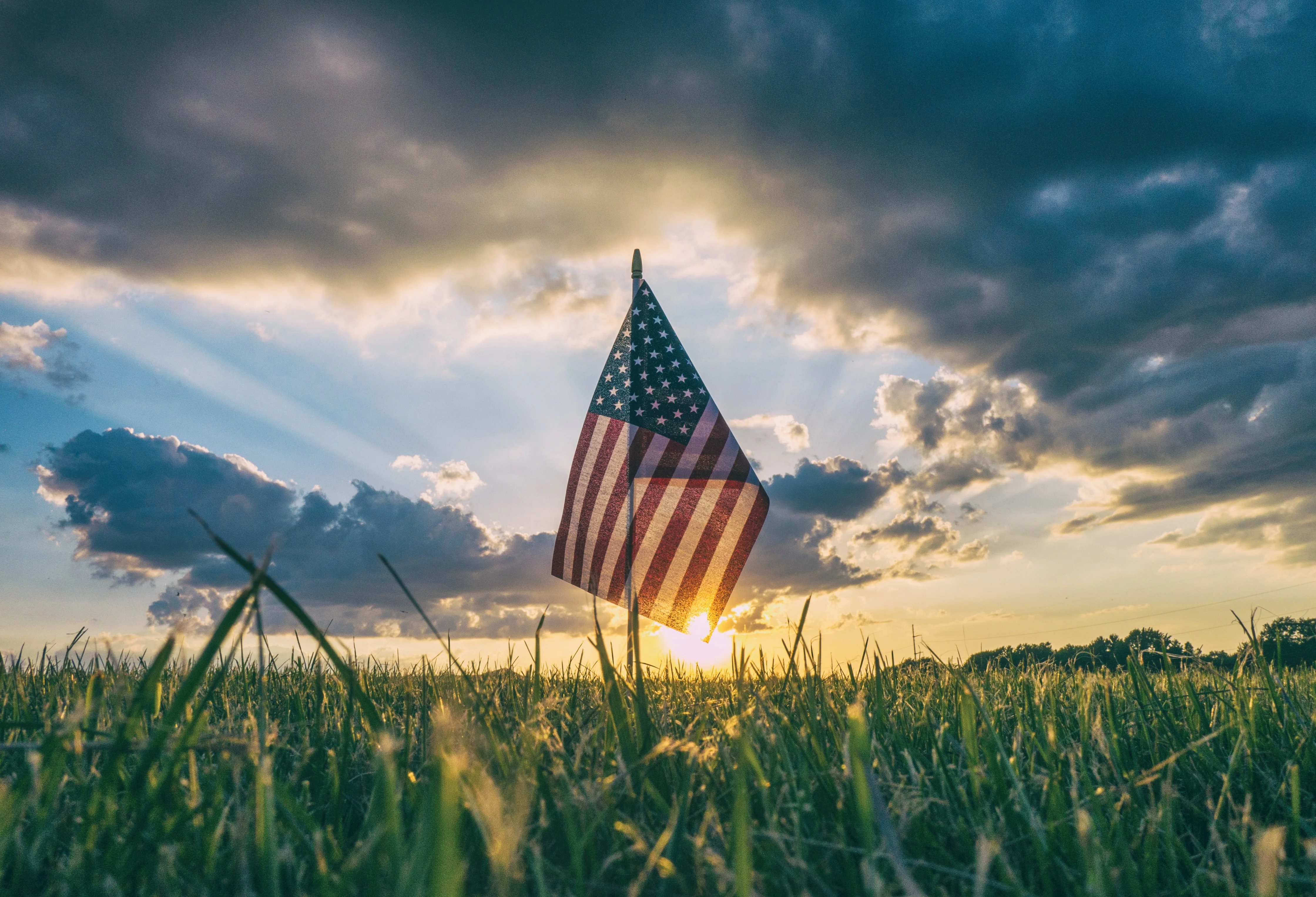 American flag planted in a field at sunset with golden light and dramatic clouds