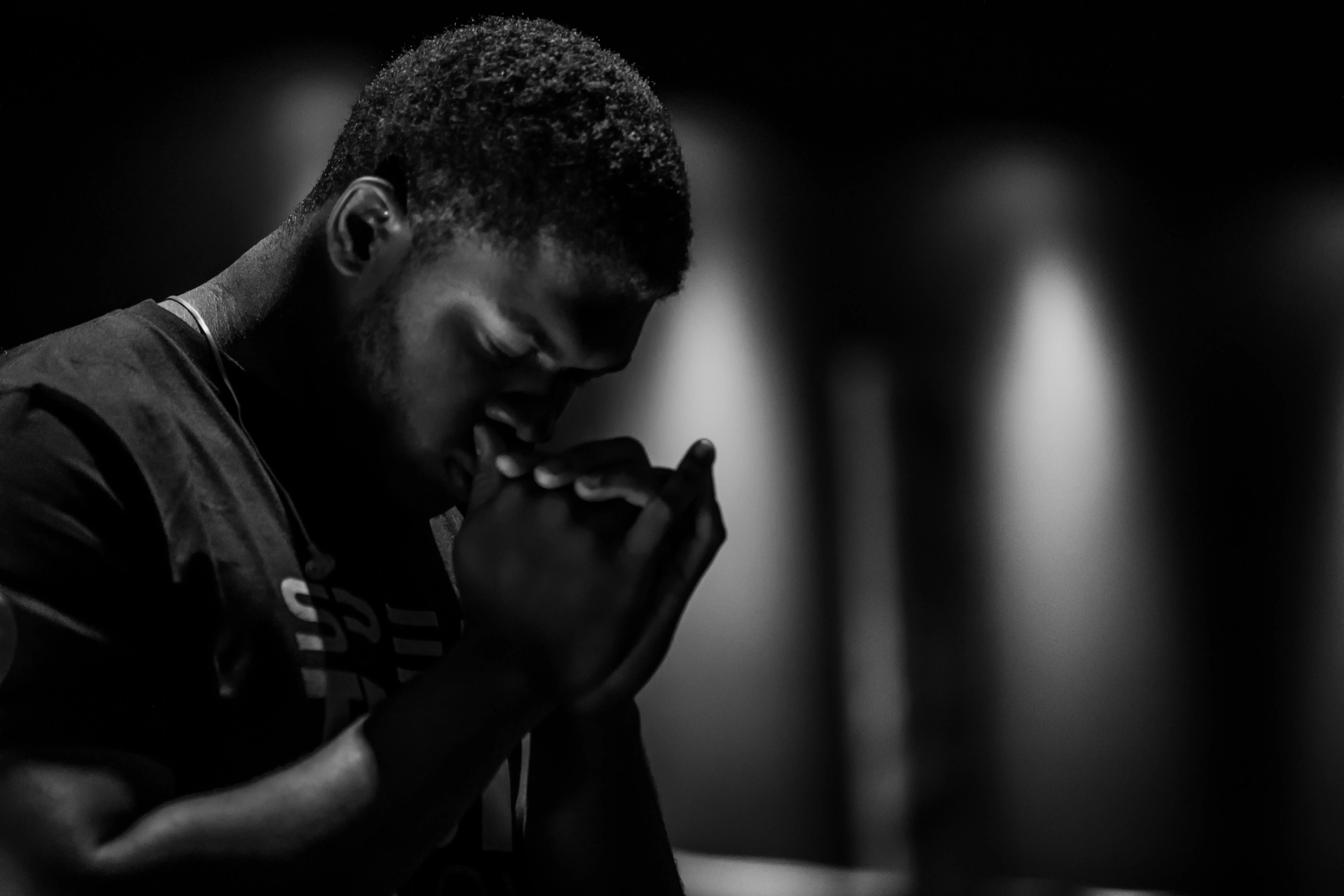 A man bowing his head in prayer, photographed in dramatic black and white with deep shadows